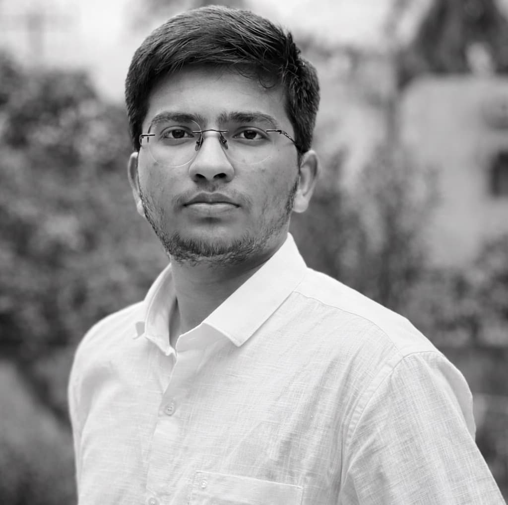 Black and white portrait of Tharak Nagaveti, in rimless glasses and a white shirt, photographed outdoors.